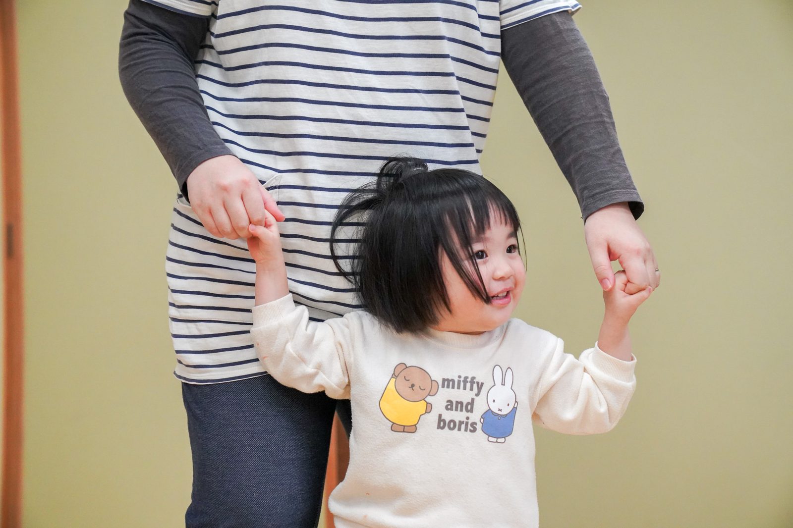 大人に手を添えてもらいながら、自分の足で歩く女の子