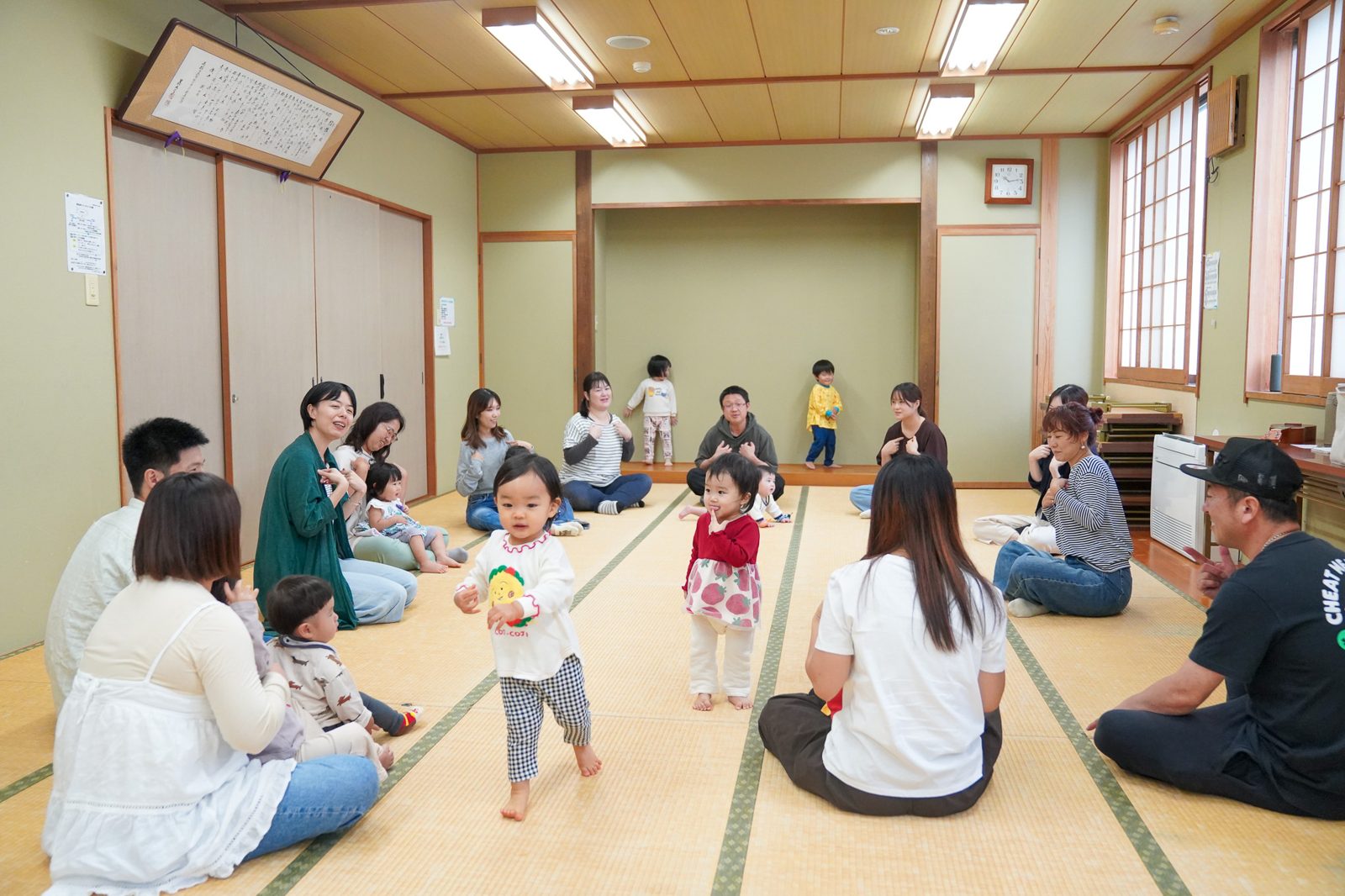 大人が輪になって座り、真ん中を子どもたちが自由に歩く様子